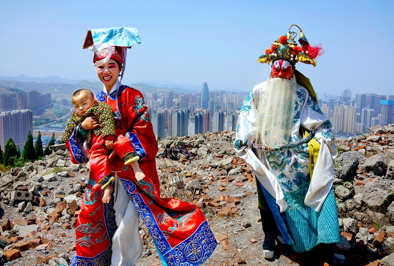 45 、《傳統(tǒng)與現(xiàn)代》2016年4月,濟(jì)南市漢峪金谷,來(lái)自魯西南的莊戶(hù)劇團(tuán)演員抱著幼子趕場(chǎng)演出。艷麗的傳統(tǒng)戲服與腳下的瓦礫形成巨大反差,而他們身后的新城已經(jīng)崛起,千年古城的時(shí)代氣息愈發(fā)濃郁。(呂廷川).JPG